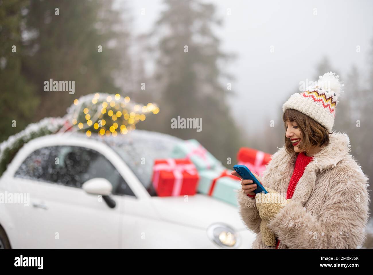 Frau mit Telefon, die mit dem Auto unterwegs ist, dekoriert für Weihnachten in den Bergen Stockfoto