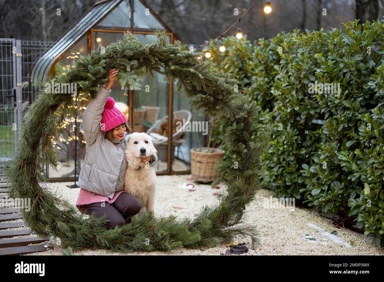 Eine Frau mit einem Hund im Weihnachtskranz im Garten Stockfoto