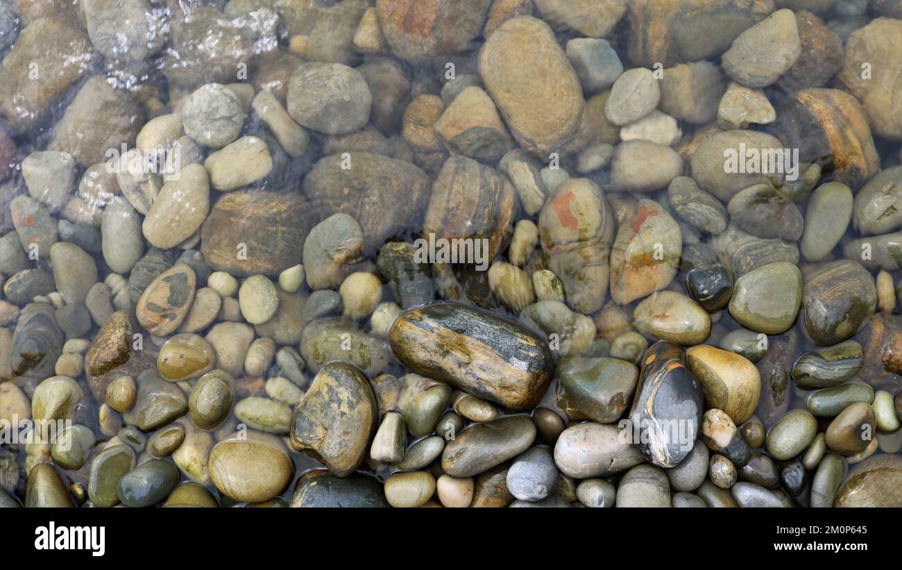 Abgerundete Textursteine in transparentem Wasser als natürlicher Hintergrund, Steinraum eines Meeres oder Flussufers in einer kleinen Menge Wasser Stockfoto