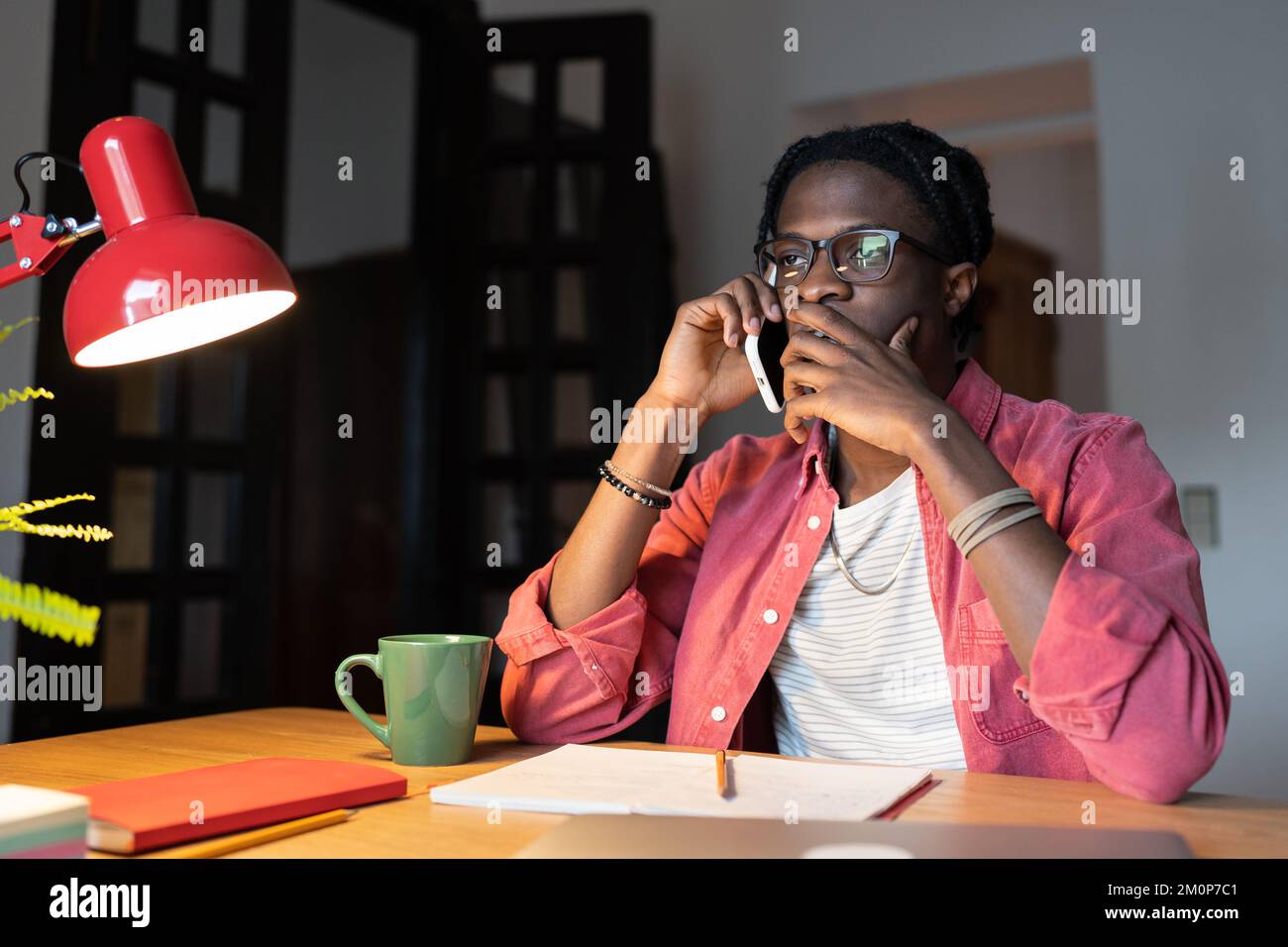 Ein besorgter, frustrierter afrikanischer Student, der telefoniert, während er zu Hause lernt Stockfoto