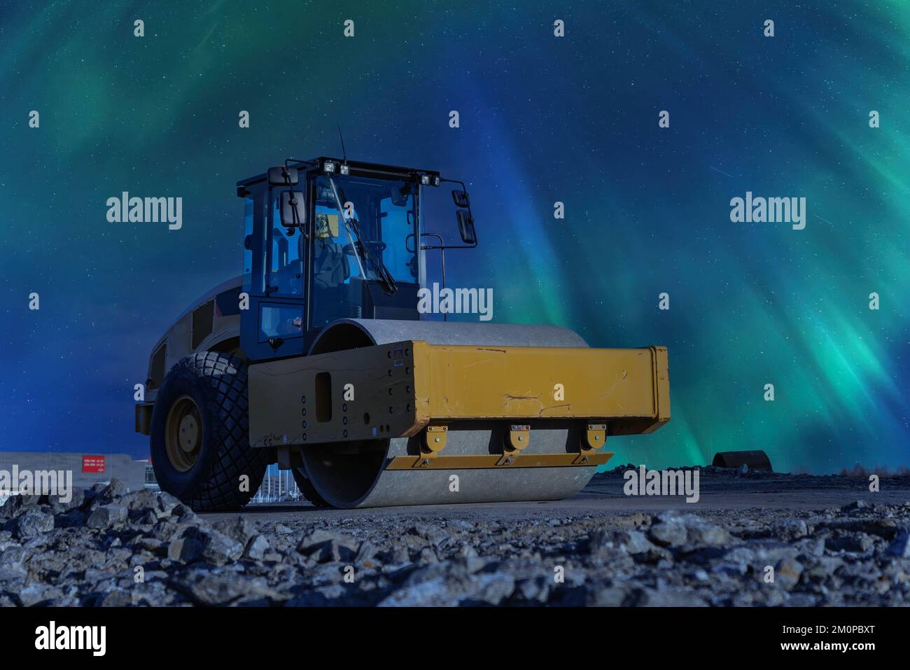 Die gelbe Straßenwalze steht auf einer nicht fertig gefertigten neuen Straße unter Early Night Aurora Borealis, Ansicht von links. Nordlichter leuchten über einem alten schweren Traktor Stockfoto