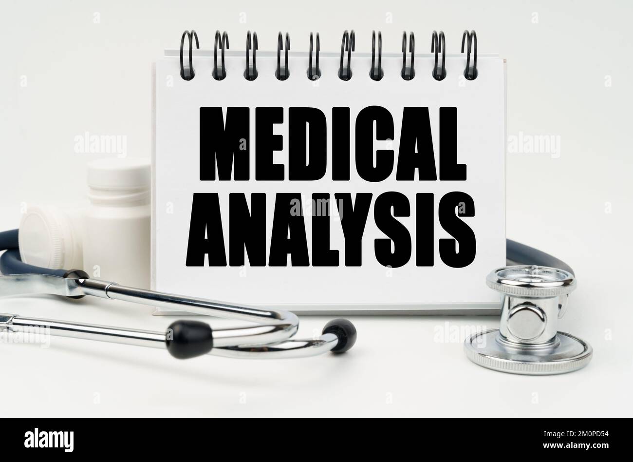 Medizin und Gesundheitskonzept. Auf einem weißen Tisch liegt ein Stethoskop, Pillen und ein Notizbuch mit der Inschrift - MEDIZINISCHE ANALYSE Stockfoto