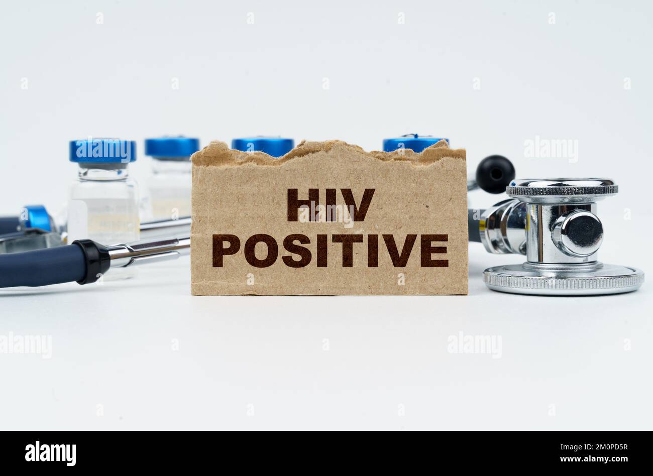 Medizin und Gesundheitskonzept. Auf einem weißen Tisch liegen Ampullen, ein Stethoskop und ein Karton mit der Inschrift - HIV-POSITIV Stockfoto