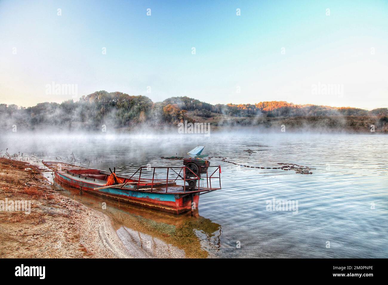 Ein frühmorgendlicher Nebel über einem Fluss mit einem alten Fischerboot im Vordergrund Stockfoto