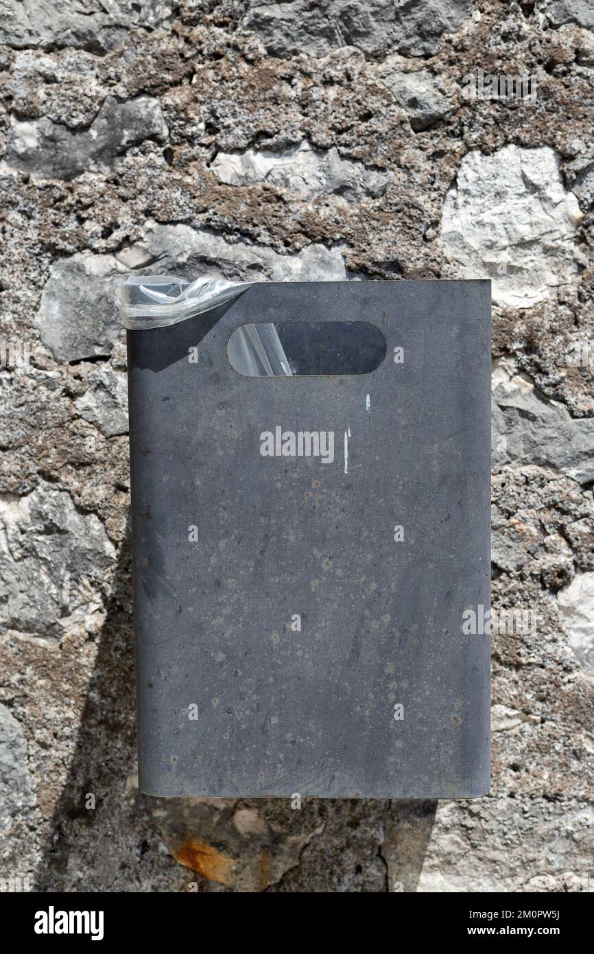Vertikales Foto eines grauen Metalltrüpfers an einer Steinwand im Hintergrund. Rechteckiger Behälter für Müll, der an der Festungswand hängt. Symmetrie. Ökologisch Stockfoto
