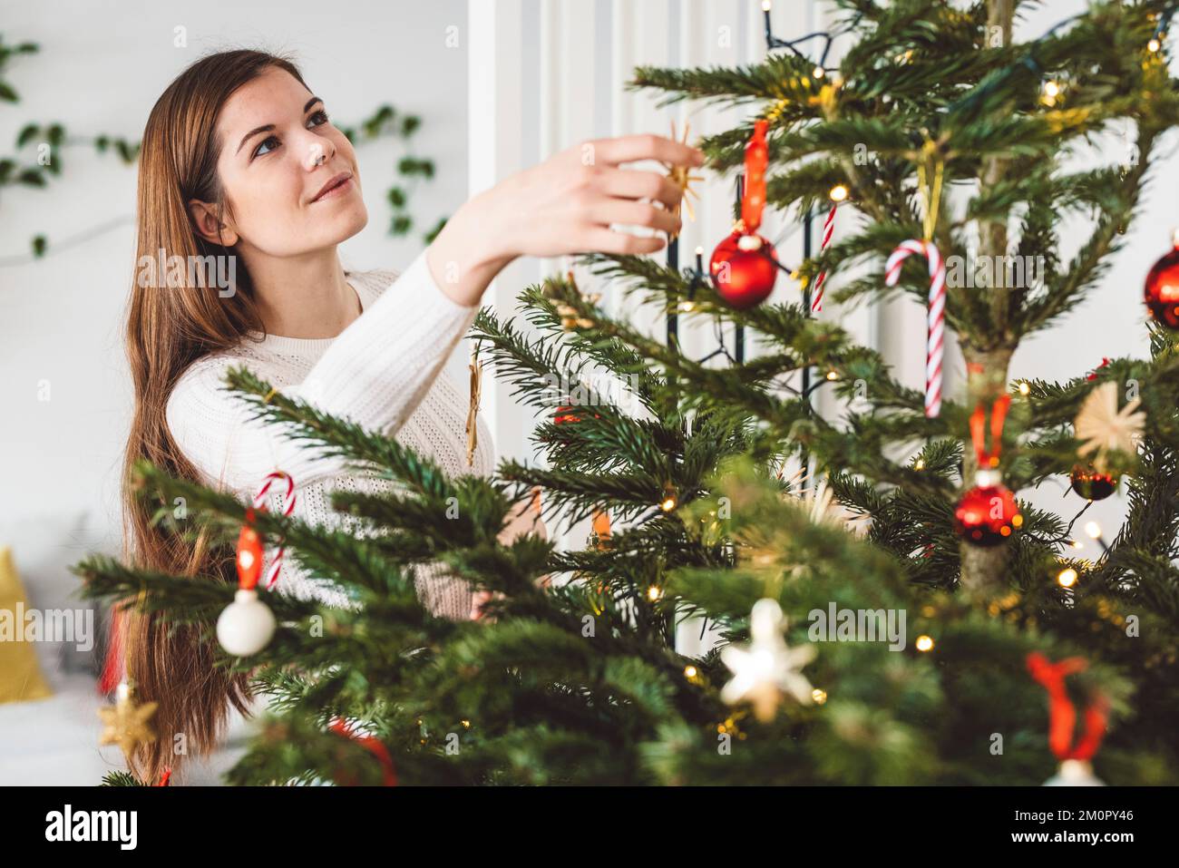 Eine lächelnde weiße Frau, die auf den natürlichen Weihnachtsbaum schaut, den sie selbst schmückt Stockfoto