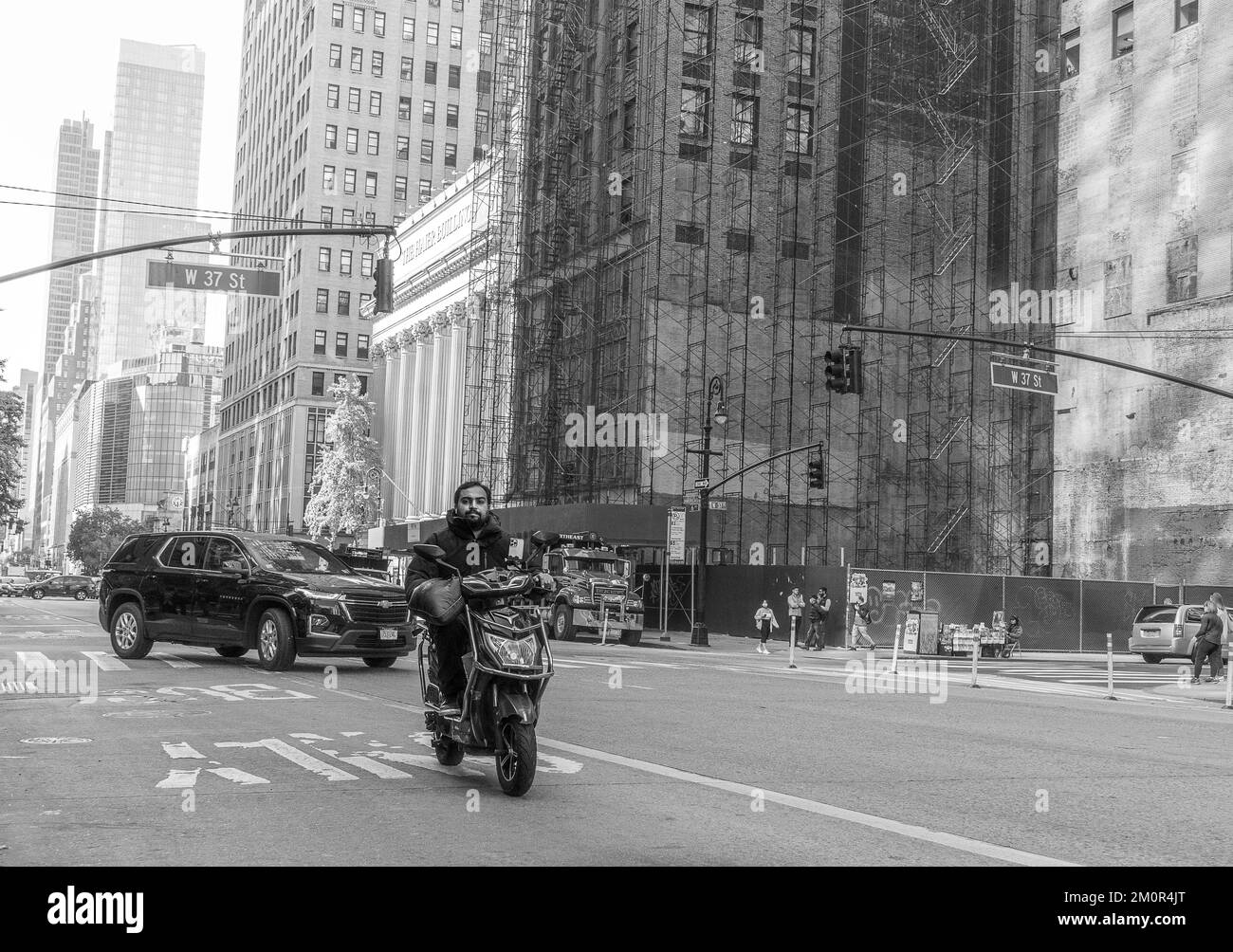 Ein asiatischer Mann fährt seinen Roller auf den Straßen von New York City mit den Wolkenkratzern von Manhattan im Hintergrund. Schwarz-weiße Straßenfotografie Stockfoto