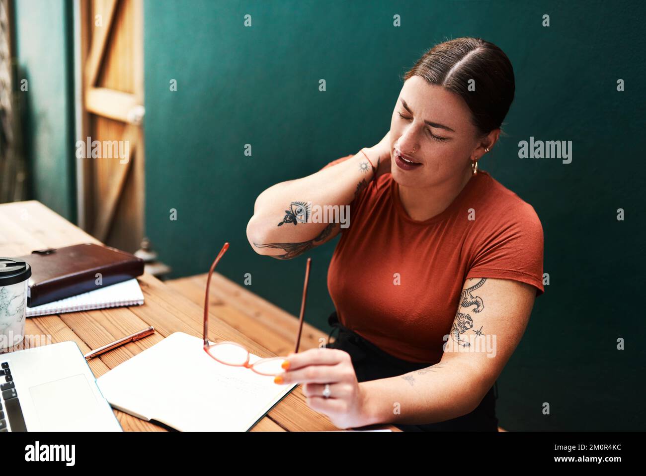 Ich habe zu lange gesessen. Eine attraktive junge Geschäftsfrau, die allein an ihrem Schreibtisch sitzt und unter Nackenschmerzen leidet. Stockfoto