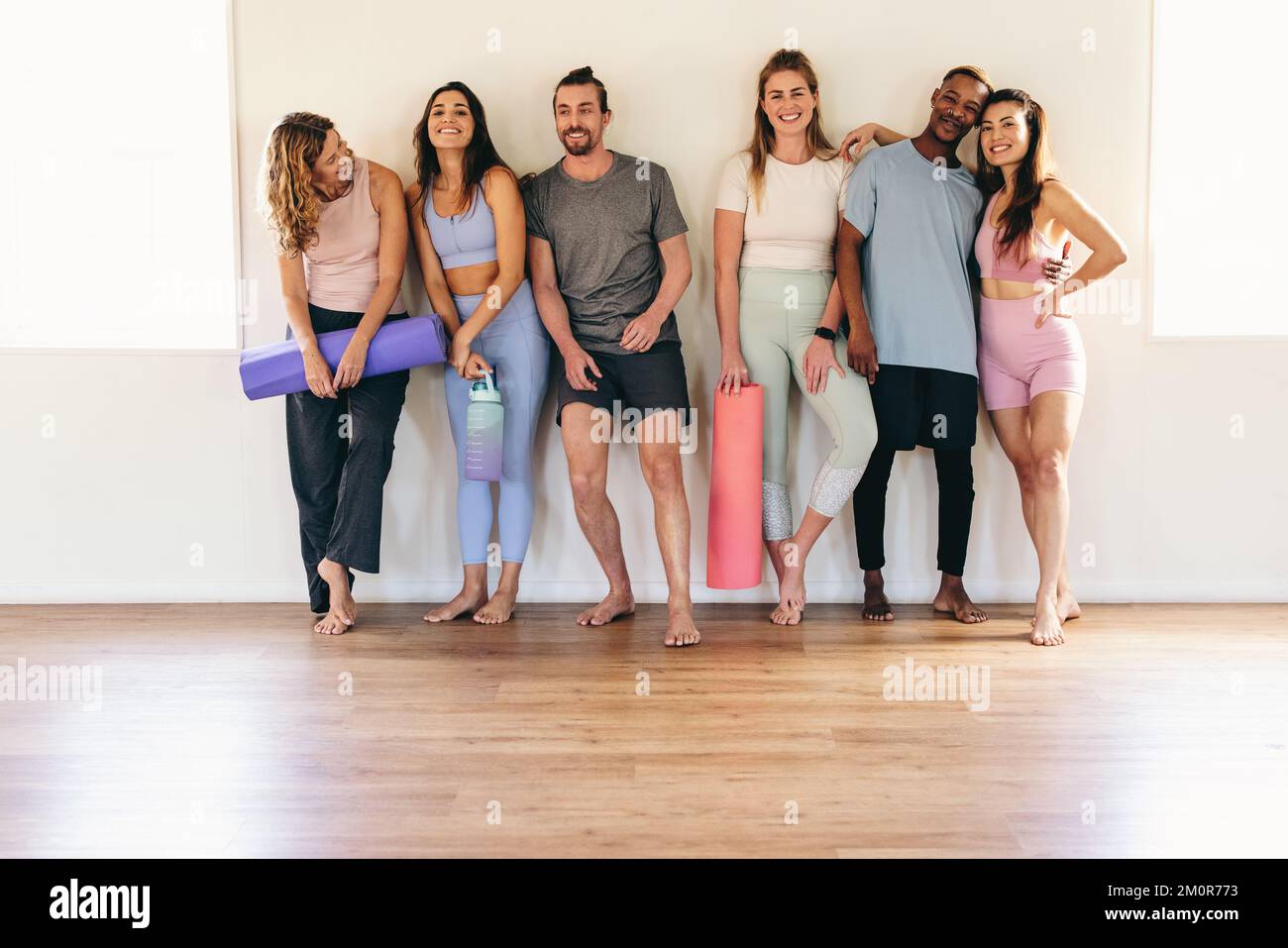 Eine Gruppe von Menschen, die mit ihren Trainingsmatten in einem Yoga-Studio lächeln und stehen. Multikulturelle Leute, die zusammen an einem Yoga-Kurs teilnehmen. Glücklich Stockfoto