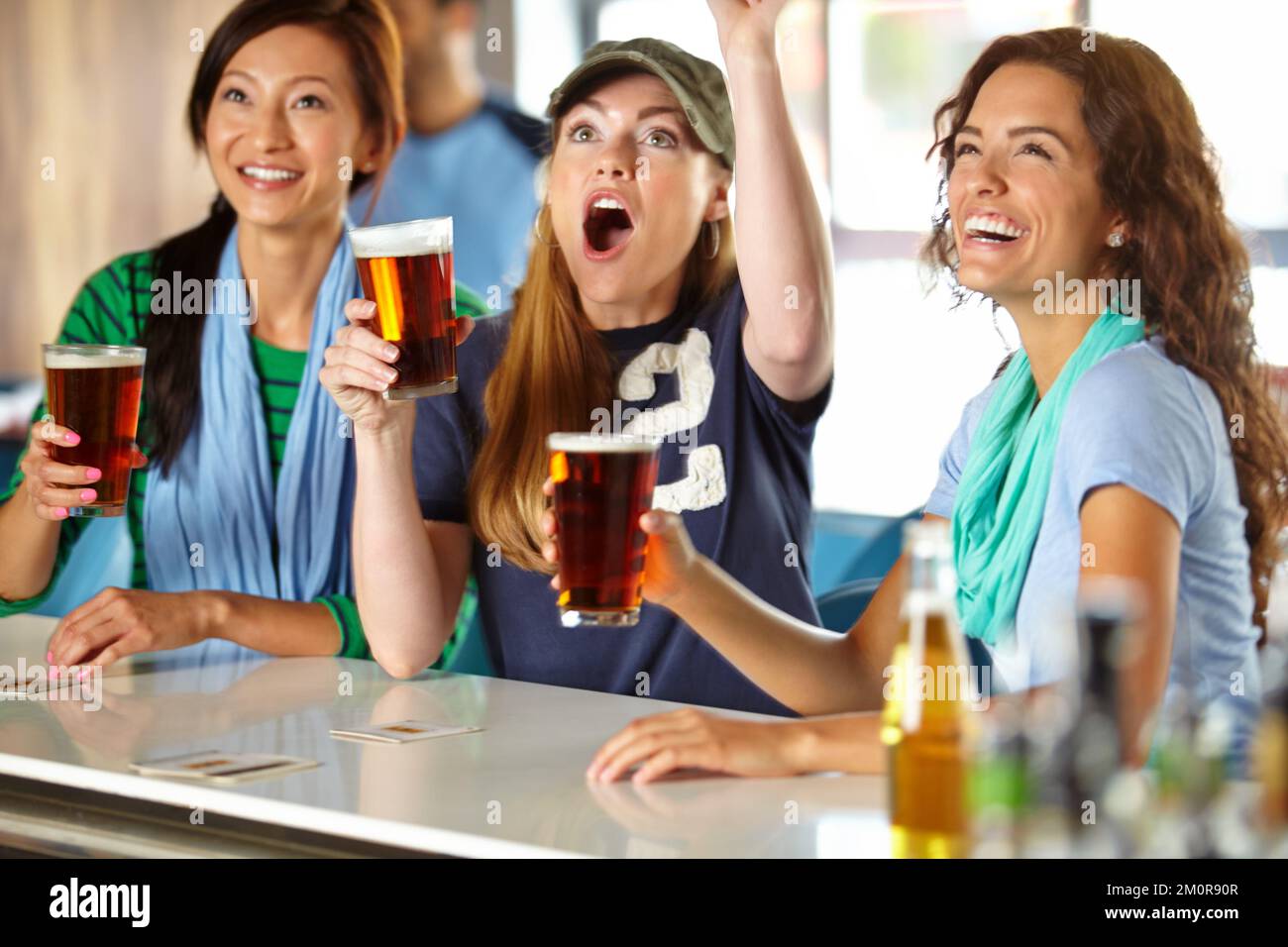 Komm schon, komm schon. Drei Freundinnen entspannen sich mit ein paar Drinks an der Bar und schauen Sport. Stockfoto