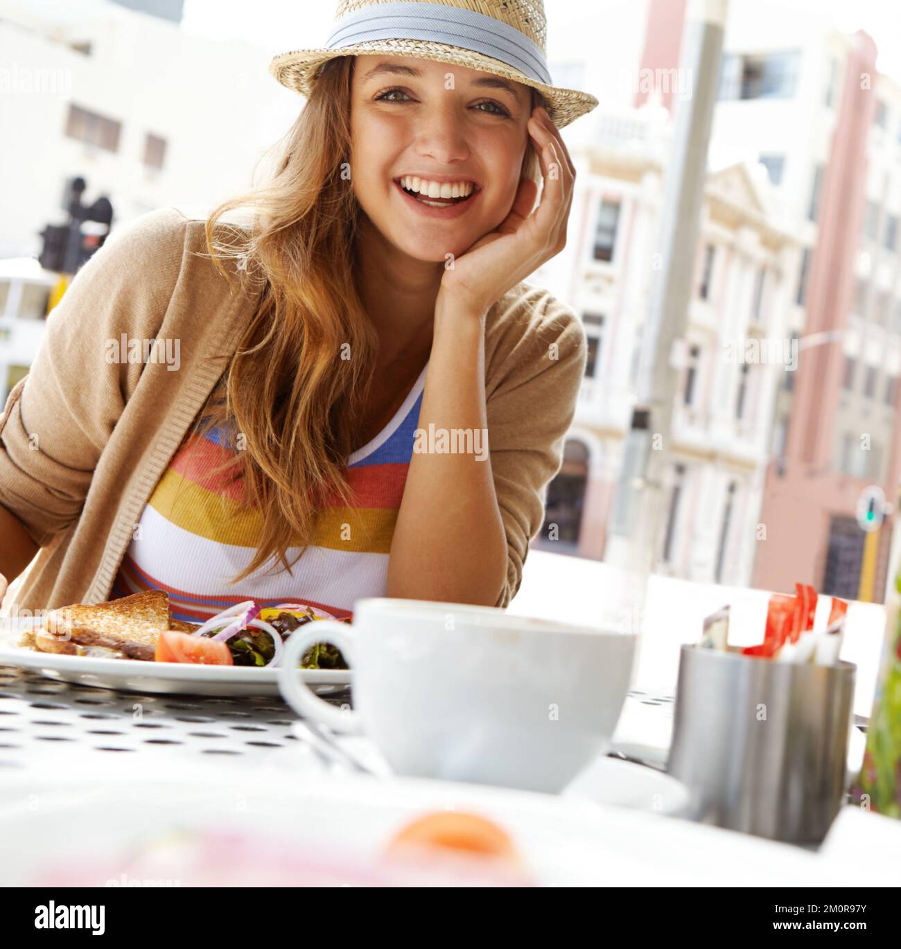 Ich genieße ein geröstetes Leckerli. Eine wunderschöne junge Frau, die eine Tasse Kaffee und ein getoastetes Sandwich in einem Straßencafé genießt - Porträt. Stockfoto