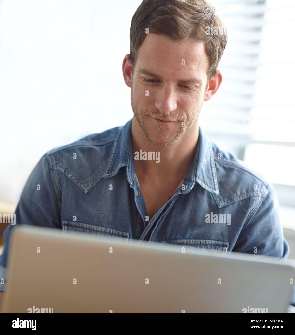 Er schickt seine Kundenliste per E-Mail. Ein gutaussehender junger Mann, der im Büro an seinem Laptop arbeitet. Stockfoto