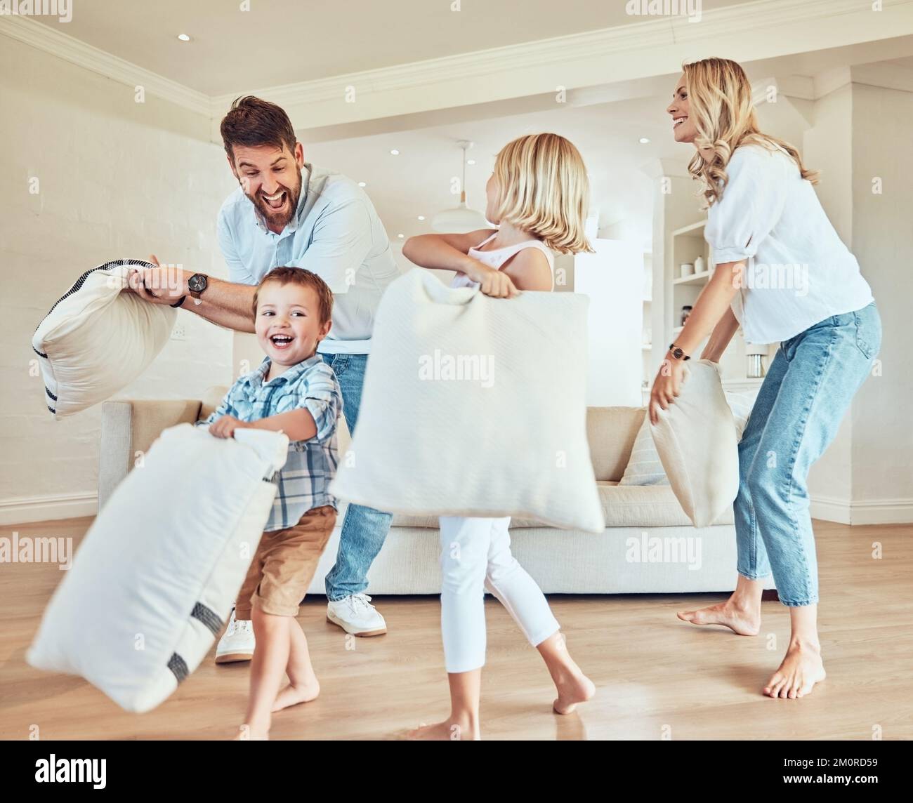 Aufgeregte Familie, die eine Kissenschlacht hat. Weiße Familie, die mit Kissen spielt. Glückliche Kinder Kissen kämpfen mit Eltern. Eltern, die sich mit ihnen anfreunden Stockfoto