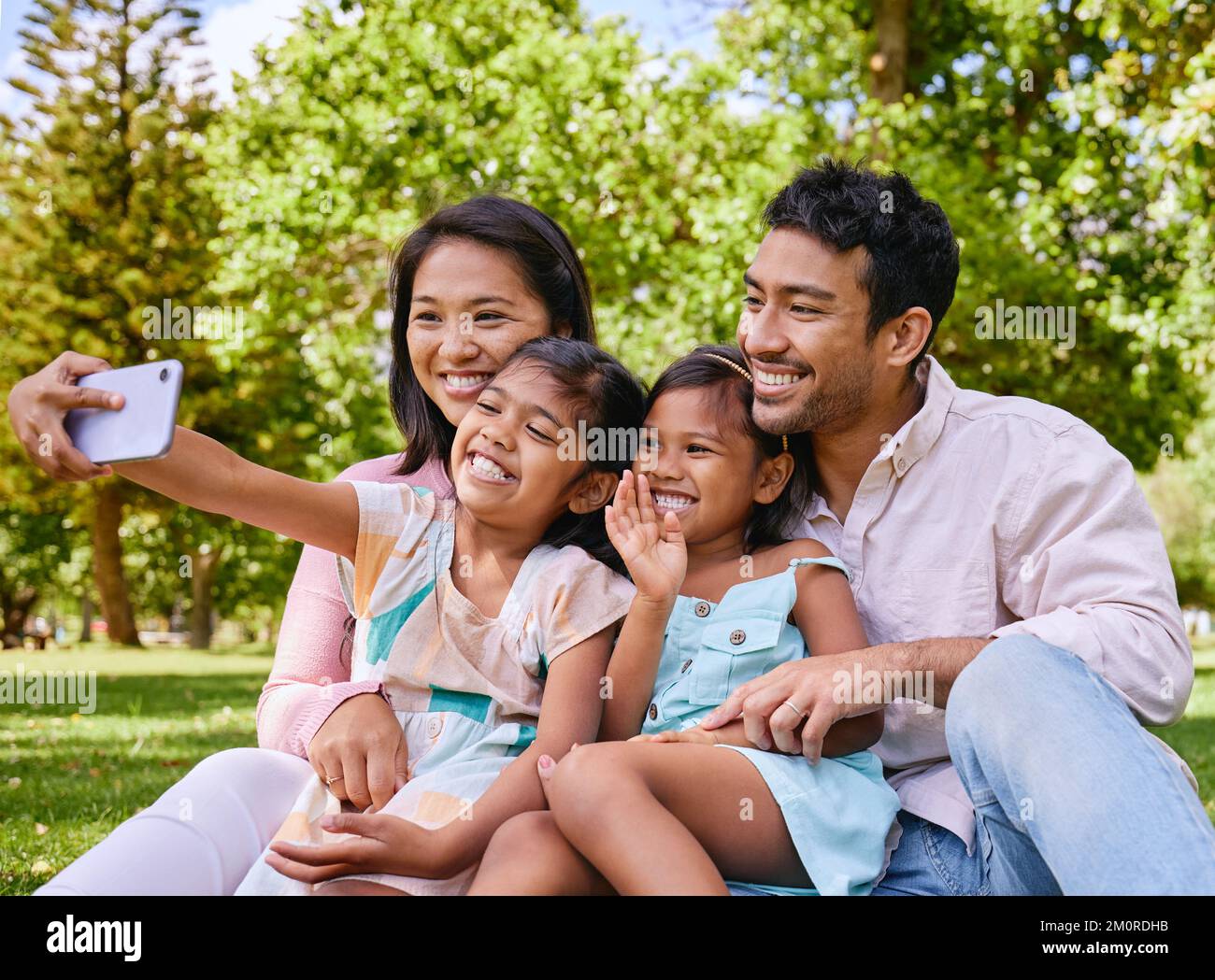 Glückliche asiatische Familie, die Selfies macht und Videogespräche führt, während sie sich im Park entspannen. Liebende Eltern, die Fotos und Bilder für eine besondere Kindheit aufnehmen Stockfoto