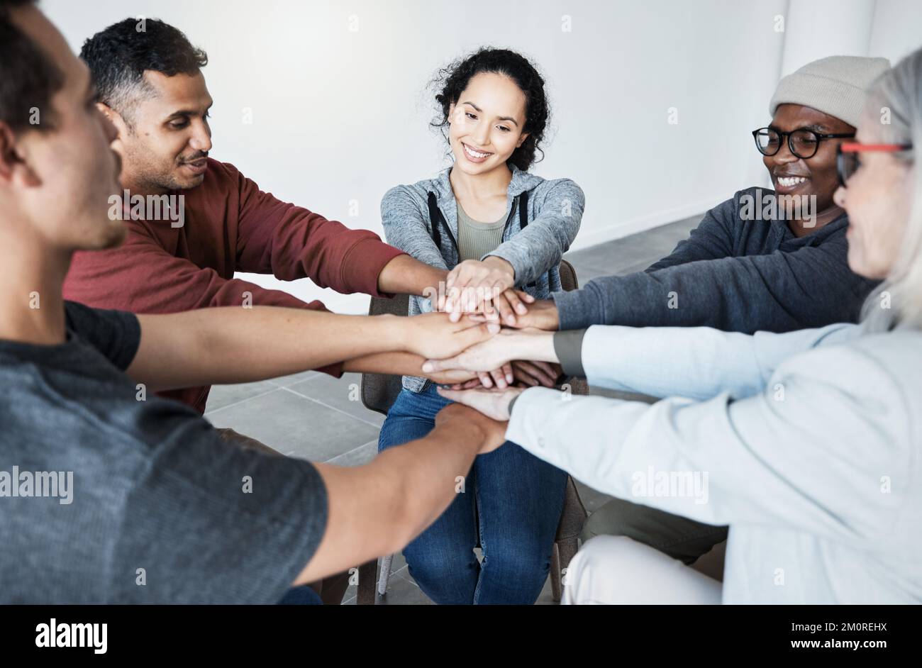 Unterschiedliche Personengruppen, die im Kreis sitzen und nach der Therapie ihre Hände in die Mitte legen. Lächelnde Selbsthilfegruppe feiert nach A Stockfoto