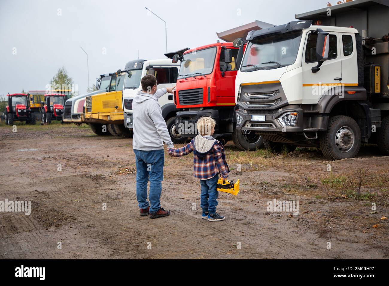 Mann und ein Junge, Vater und Sohn, stellt euch mit dem Rücken vor große Lastwagen. Die Leidenschaft des Kindes für Autos, Vater und Kind, schaut euch die Autos im Pa an Stockfoto