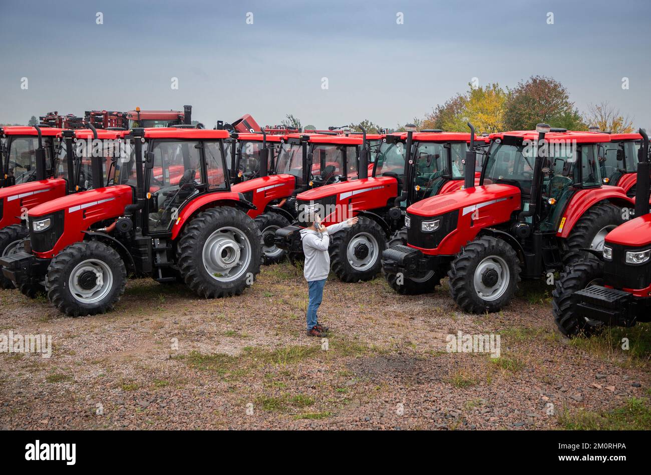 Präsentation und Verkauf neuer roter Traktoren in Folge. Ein Mann spricht am Telefon und zeigt auf einen der landwirtschaftlichen Traktoren. Ausrüstung für einen Stockfoto