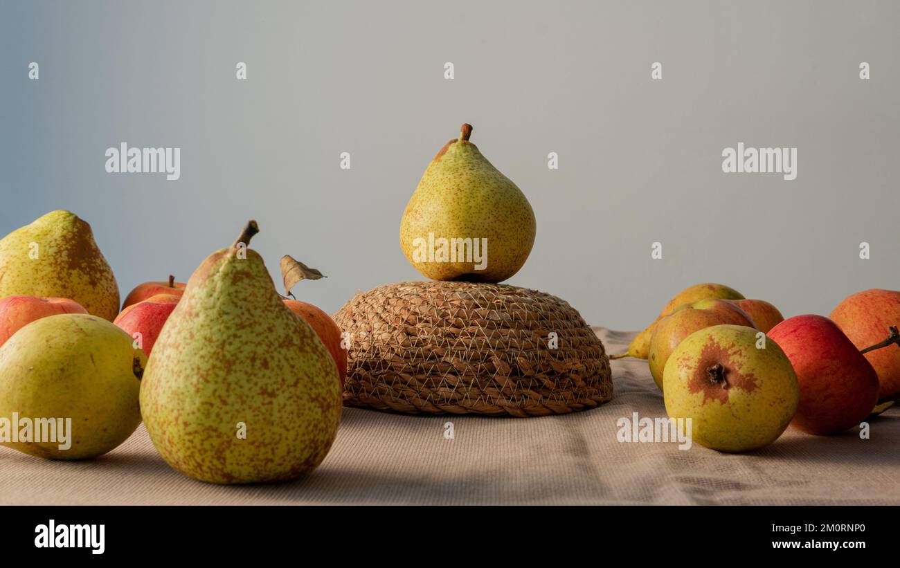 Birnen und Äpfel auf einem Tisch mit einer Birne auf einem umgedrehten Rattankorb Stockfoto