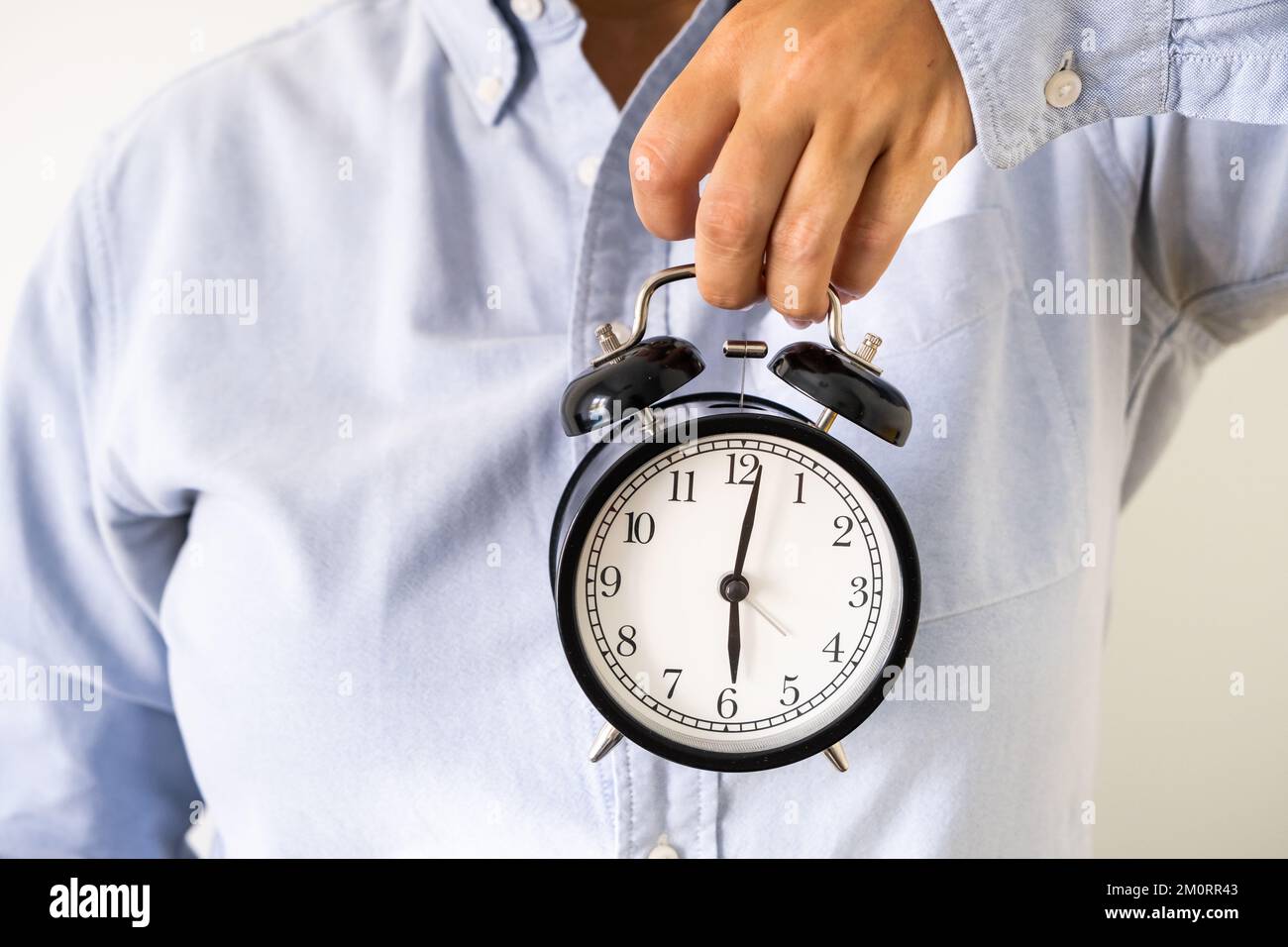 Die Hand einer Frau in Bürokleidung hält um sechs Uhr morgens einen Wecker Stockfoto