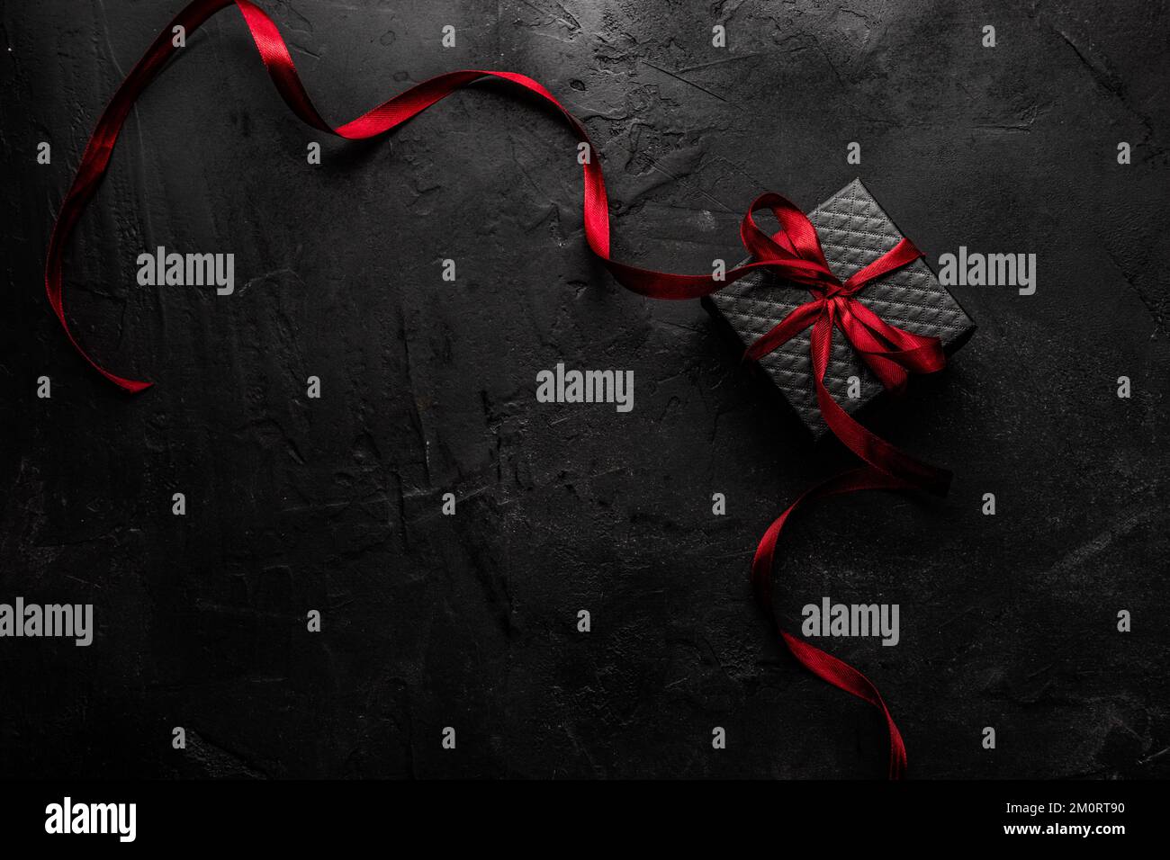 Ansicht einer schwarzen Geschenkbox mit einem roten Band auf schwarzem Hintergrund von oben Stockfoto