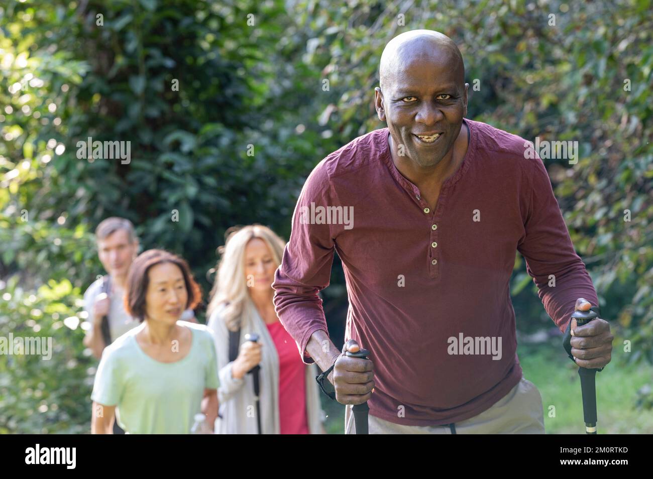 Älterer afroamerikanischer Mann, der Wanderstöcke hält und mit einer Gruppe von verschiedenen älteren Freunden eine Wanderung macht Stockfoto