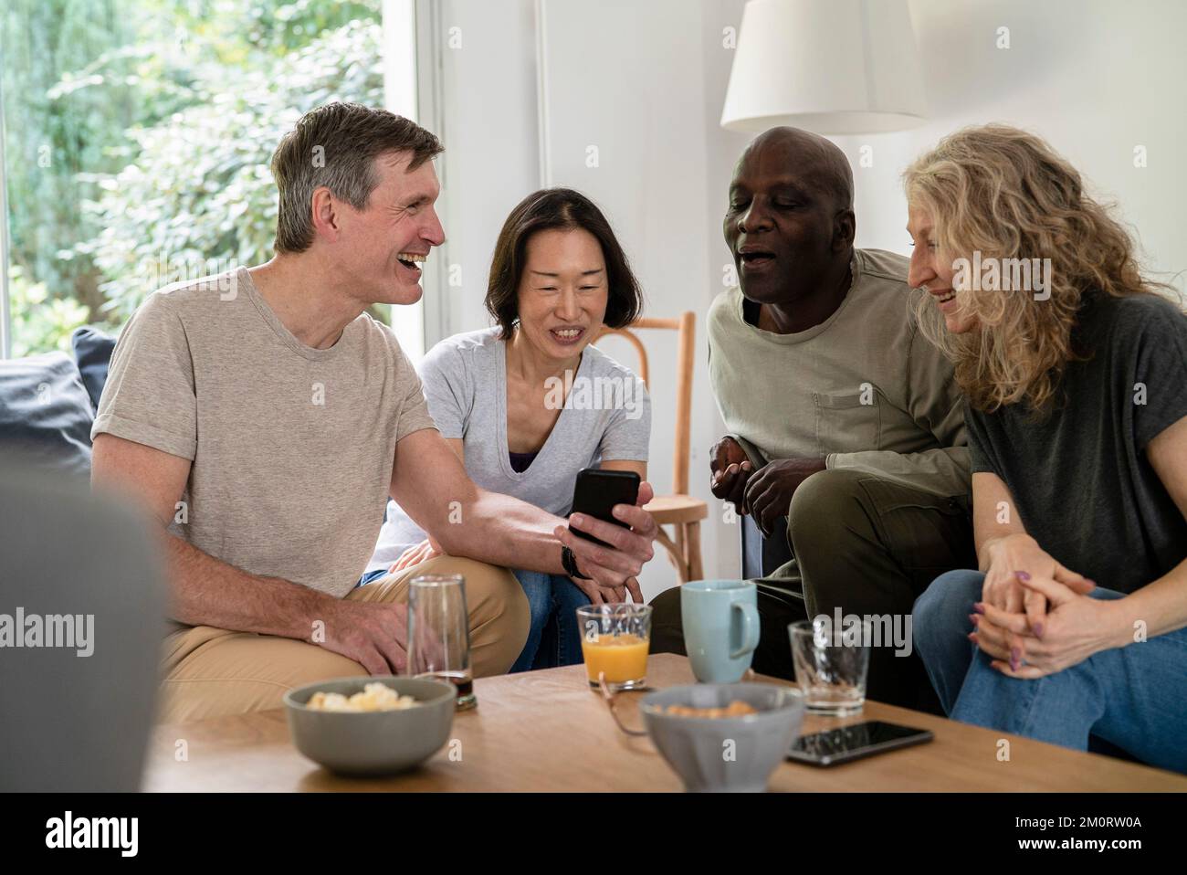 Seniorenpaare versammelten sich im Wohnzimmer, während sie sich das Smartphone anschauten Stockfoto