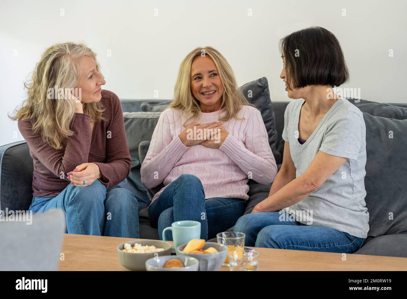 Drei ältere Freundinnen unterhalten sich, während sie zu Hause auf dem Sofa sitzen Stockfoto