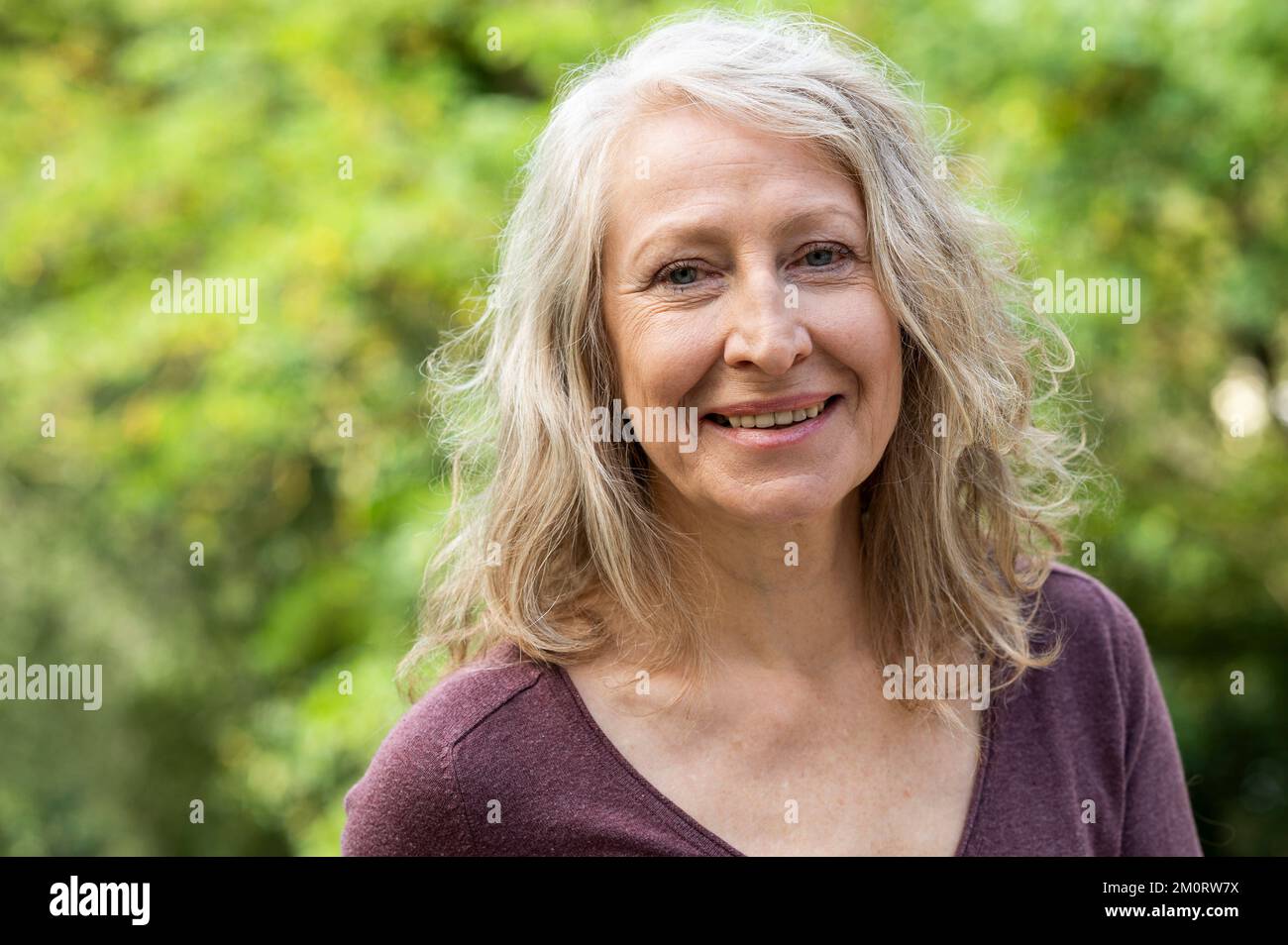 Porträt einer Dame mittleren Alters, die in die Kamera schaut, während sie draußen im Garten sitzt Stockfoto