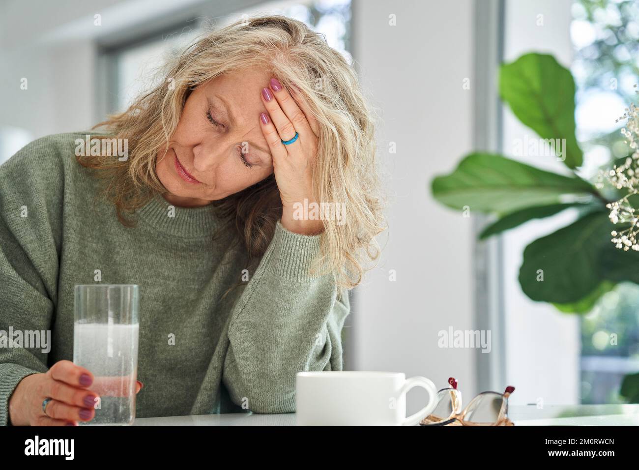 Ältere Frau, die im Esszimmer Kopfschmerzen hat Stockfoto