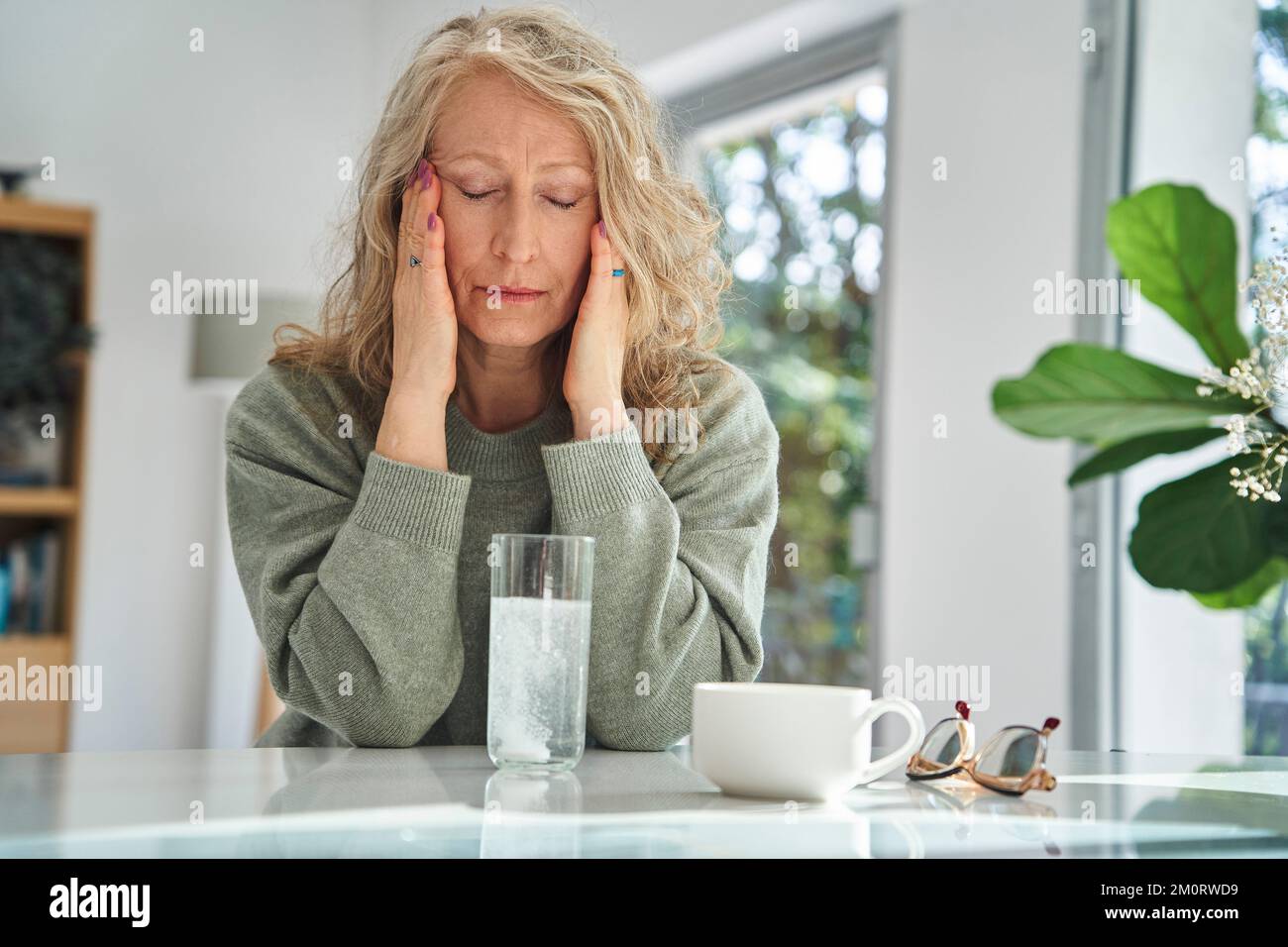 Gestresste Seniorin, die ihr Gesicht berührt, während sie Medizin trinkt Stockfoto