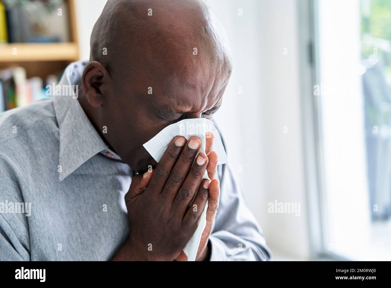 Nahaufnahme eines älteren afroamerikanischen Mannes mit einer Erkältung, die ihm die Nase bläst Stockfoto