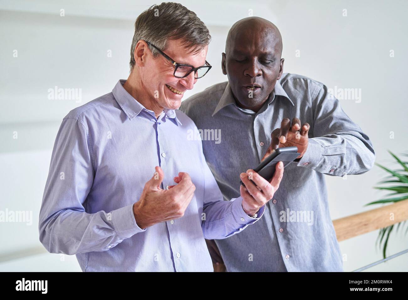 Zwei ältere, heterogene männliche Freunde, die sich zu Hause Fotos auf dem Handy ansehen Stockfoto