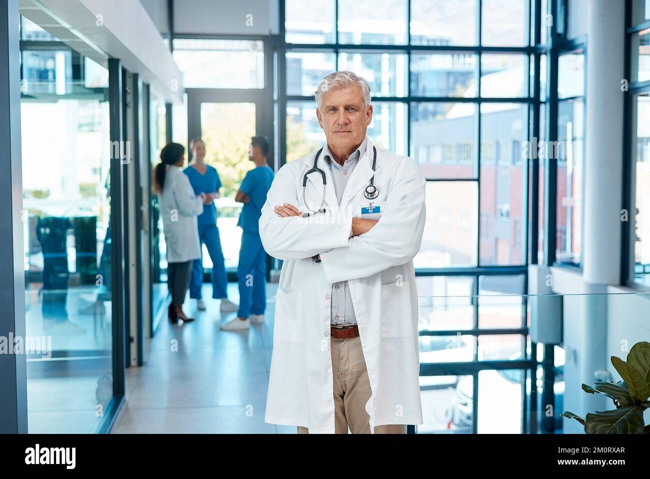 Ihre Gesundheit steht an erster Stelle. Ein reifer, männlicher Arzt, der mit gekreuzten Armen in einem modernen Krankenhaus steht. Stockfoto