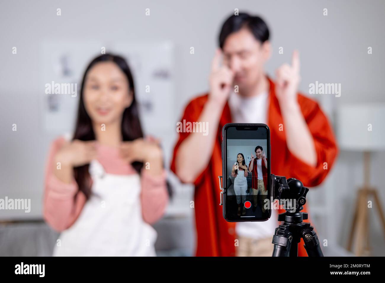 Ein asiatisches junges Paar Tiktoker kreiert sein Tanzvideo mit Smartphone-Kamera und Stativ. Niedlicher Mann und niedliche Frau, die ein vertikales Video erstellen, um es in sozialen Medien zu teilen Stockfoto