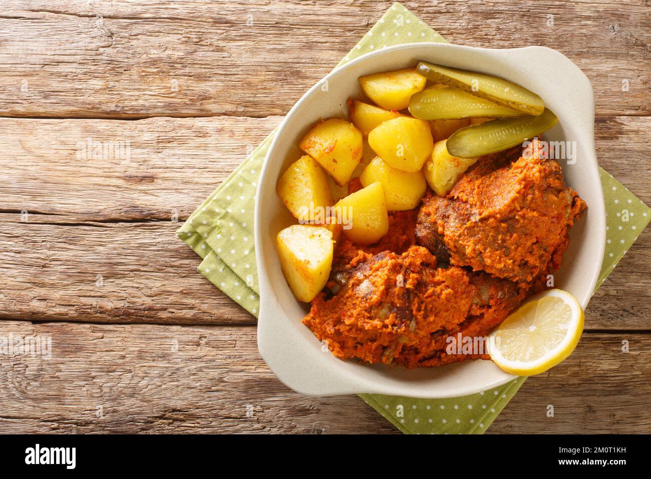 Hähnchenteile, gebacken in scharfer Sauce mit Kartoffeln, afrikanisches Hühnchen im macau-Stil, aus nächster Nähe in einem Topf auf einem Holztisch. Horizontale Draufsicht von oben Stockfoto
