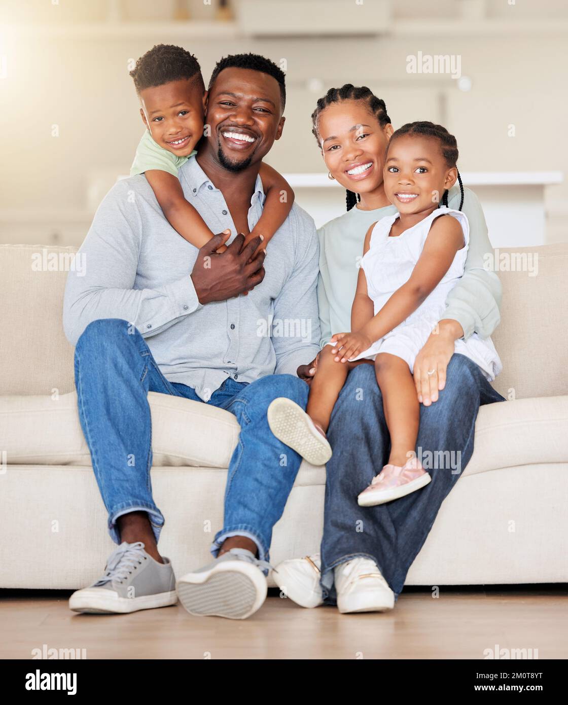 Porträt einer glücklichen afroamerikanischen Familie mit zwei Kindern, die zu Hause auf der Couch sitzen. Liebenswert kleines Mädchen und Junge sitzen mit ihrer Mutter und Stockfoto