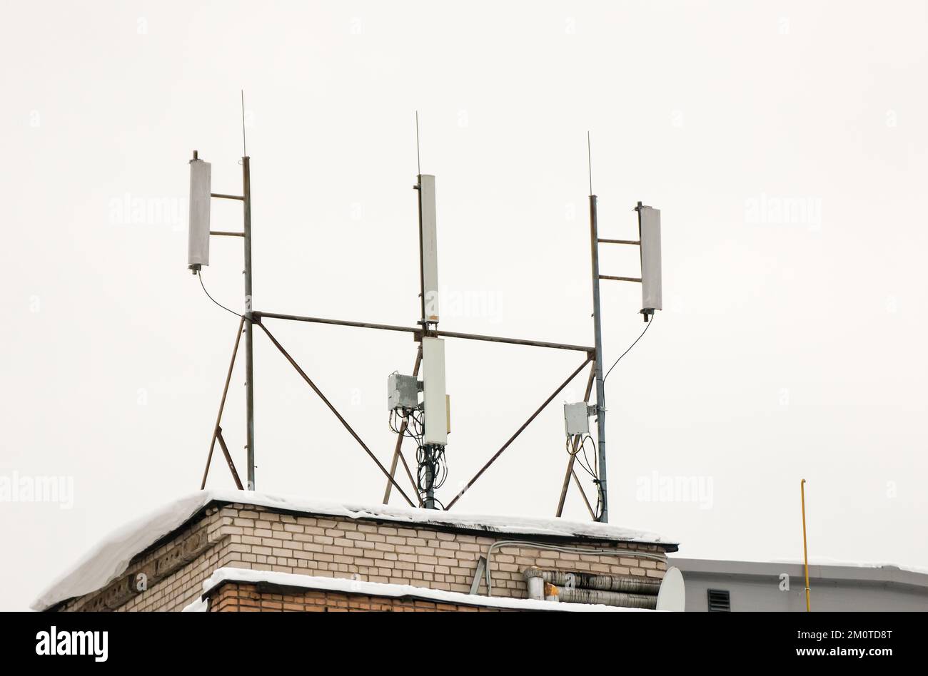 Mehrere Mobilfunkantennen auf dem Dach des Hauses sorgen für Kommunikation. Schnee liegt auf dem Meilenstein, vor dem Hintergrund eines grauen Himmels. Bewölkt, kalter Wintertag, weiches Licht. Stockfoto