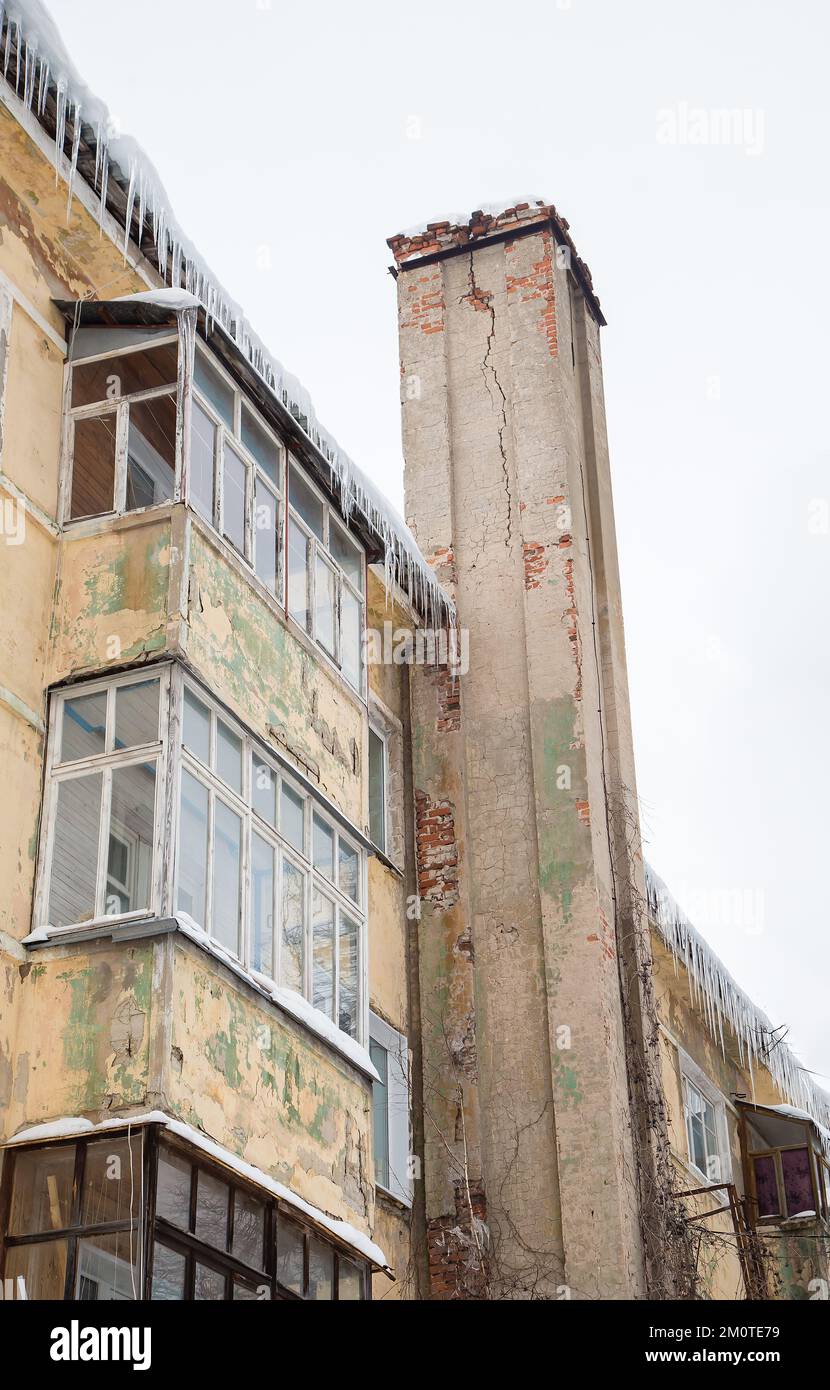 Gefährliche, schmelzende Eiszapfen hängen im Frühling oder Winter am Dachrand. Wand eines alten Backsteinhauses mit Fenstern. Große Eiszapfen in glatten, schönen Reihen. Bewölkter Wintertag, weiches Licht. Stockfoto