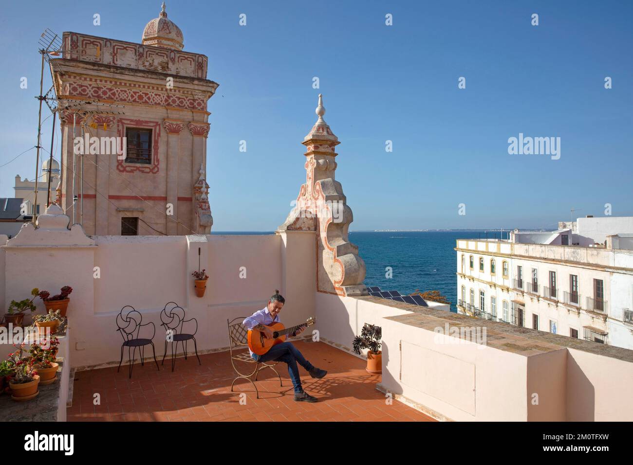 Spanien, Andalusien, Cadiz, Casa de las cuatro torres, Flamenco-Gitarrist, der auf einem Stuhl von der Terrasse eines Einkaufsturms aus dem 18.. Jahrhundert spielt und in ein Boutique-Hotel mit Blick auf das Meer umgewandelt wurde Stockfoto