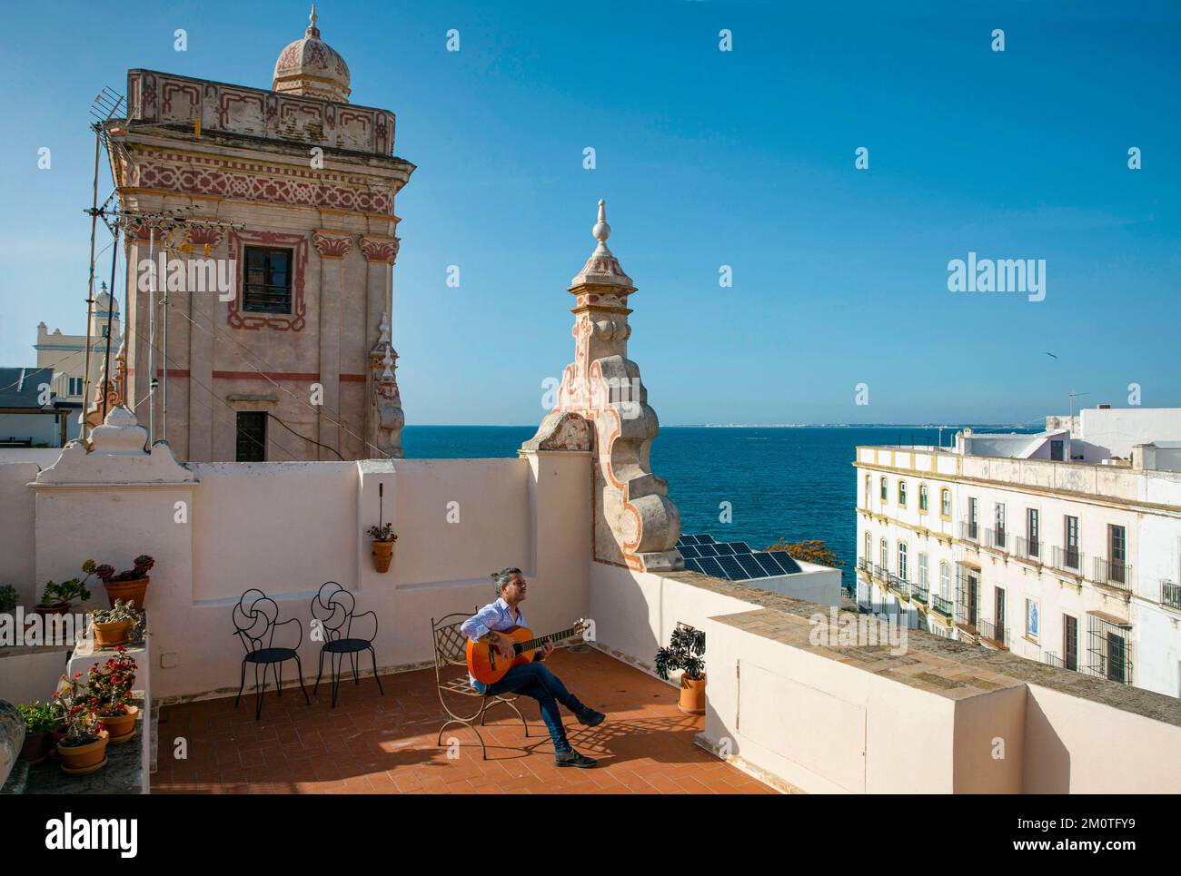 Spanien, Andalusien, Cadiz, Casa de las cuatro torres, Flamenco-Gitarrist, der auf einem Stuhl von der Terrasse eines Einkaufsturms aus dem 18.. Jahrhundert spielt und in ein Boutique-Hotel mit Blick auf das Meer umgewandelt wurde Stockfoto