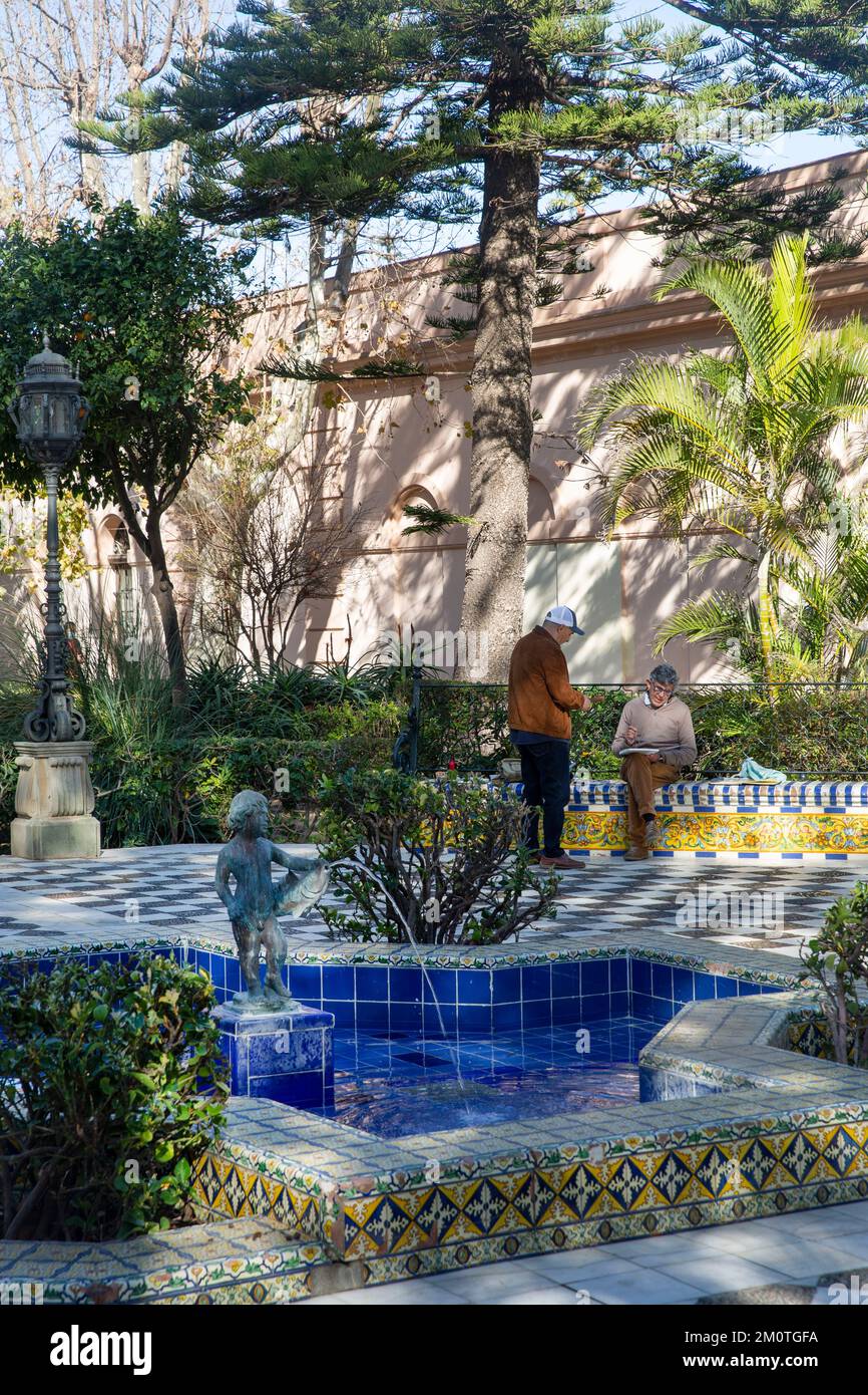 Spanien, Andalusien, Cadiz, Alameda Apodaca, Wasserkoloristen sitzen auf einer mit Azuleros geschmückten Bank entlang der von Bäumen gesäumten Promenade am Meer Stockfoto