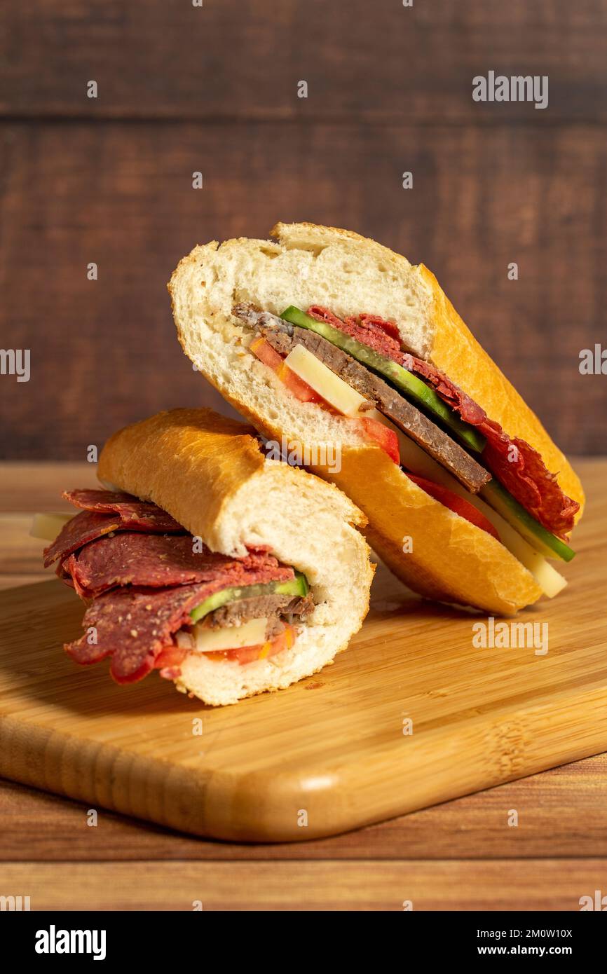 Baguette-Sandwich. Sandwich mit Salami, Roastbeef, Cheddar, Tomaten und Gurke auf Holzhintergrund Stockfoto