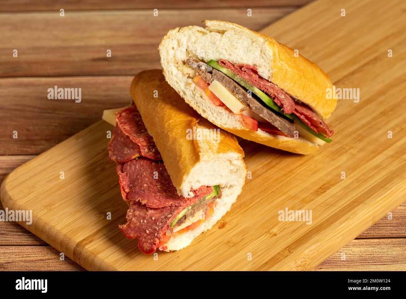 Baguette-Sandwich. Sandwich mit Salami, Roastbeef, Cheddar, Tomaten und Gurke auf Holzhintergrund Stockfoto