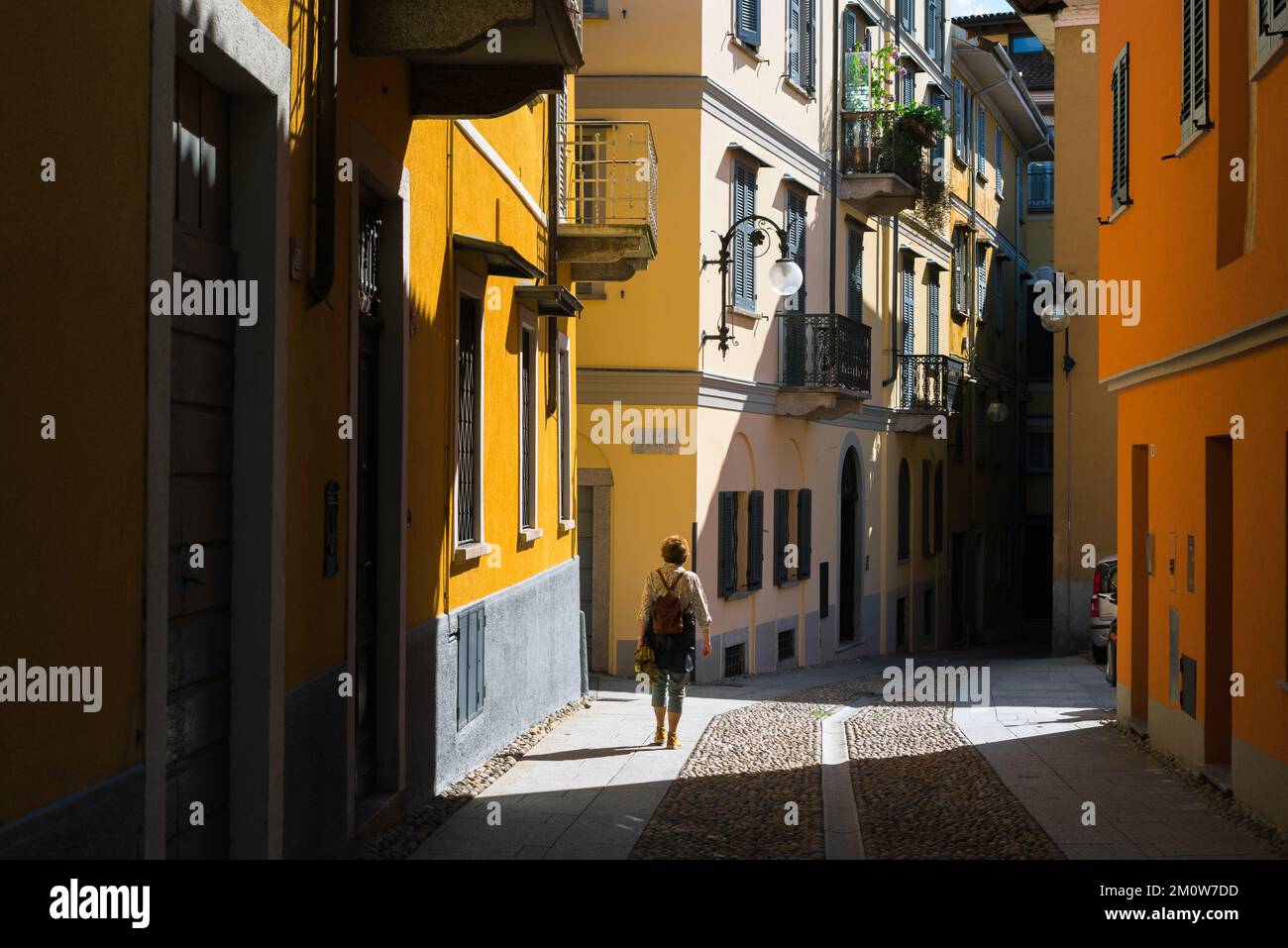 Reisen Sie nach Italien, sehen Sie im Sommer eine Frau mit Rucksack, die eine farbenfrohe Straße in der Stadt Pallanza im Lago Maggiore, Piemont, Italien, erkundet Stockfoto