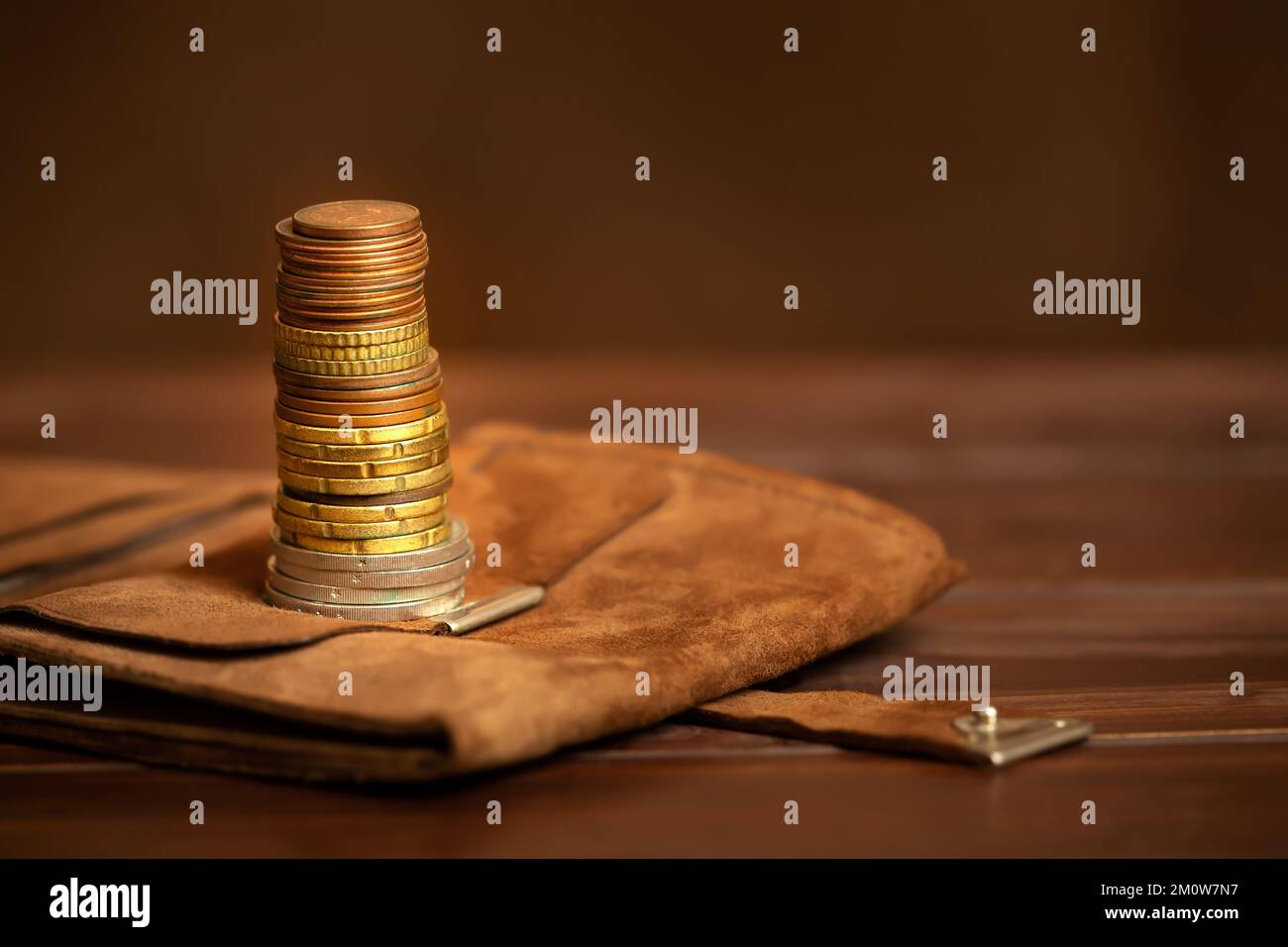 Goldmünzen stapeln sich auf einer Brieftasche auf braunem Hintergrund. Geschäftserfolg, Lösung oder Finanzdienstleistungen. Vermögensverwaltung, Private Banking. Stockfoto