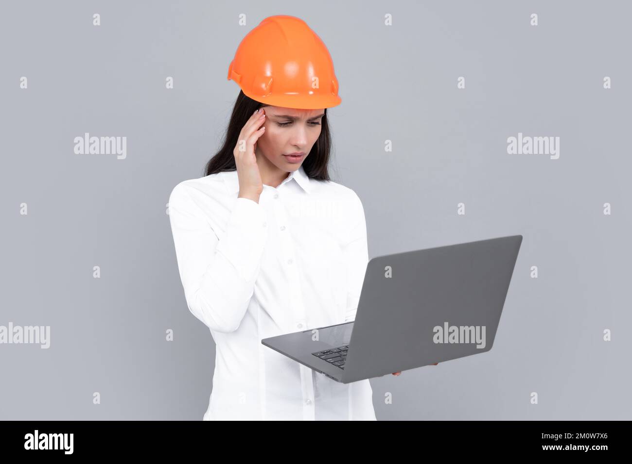 Eine Geschäftsfrau mit Laptop, Porträt auf Grau. Porträt einer Arbeiterin im Helm. Stockfoto