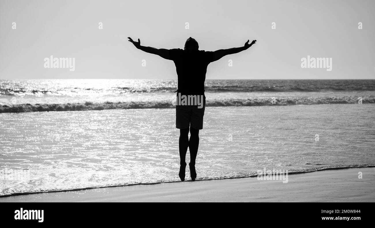 Gesunder Mann Silhouette hob die Hände am Strand. Energischer Sommer. Fühlen Sie Freiheit. Stockfoto