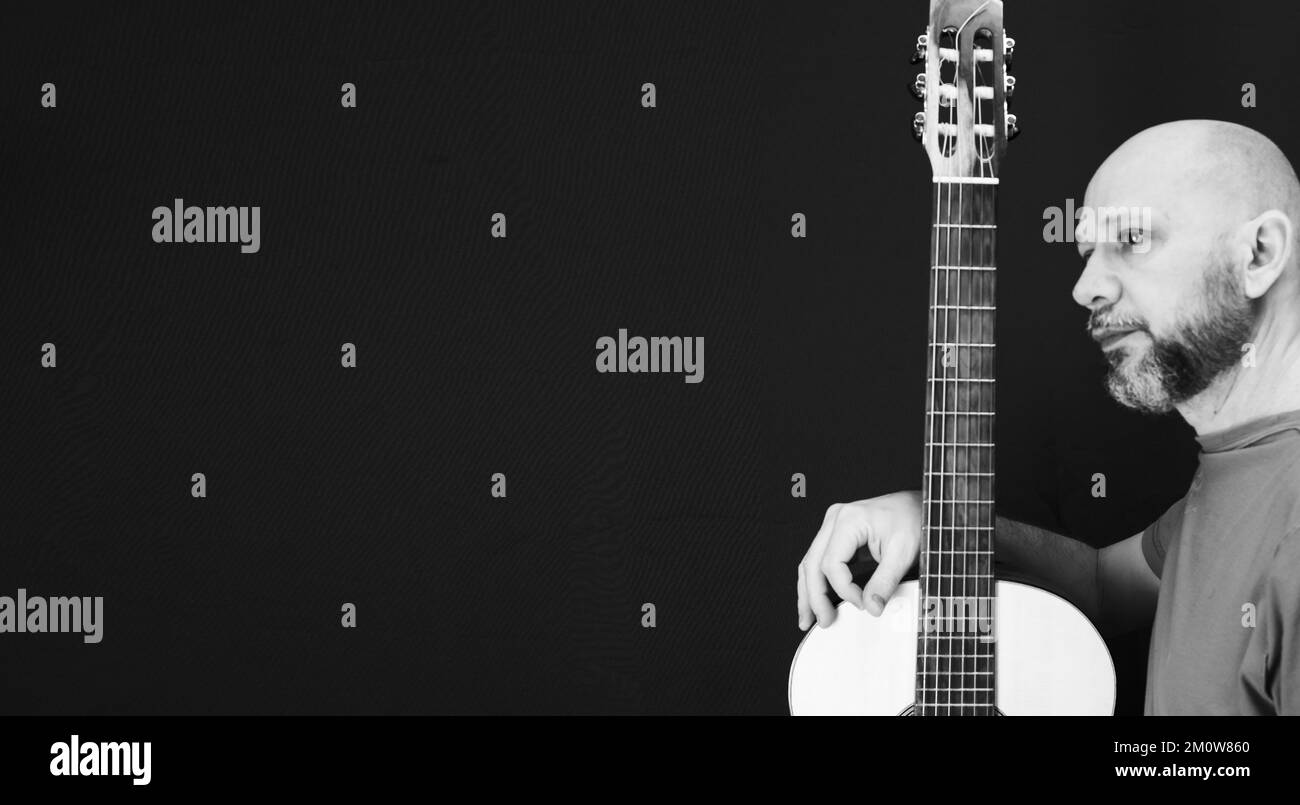 Ein charismatischer männlicher Gitarrist, isoliert auf dunklem Hintergrund, Graustufenbild Stockfoto