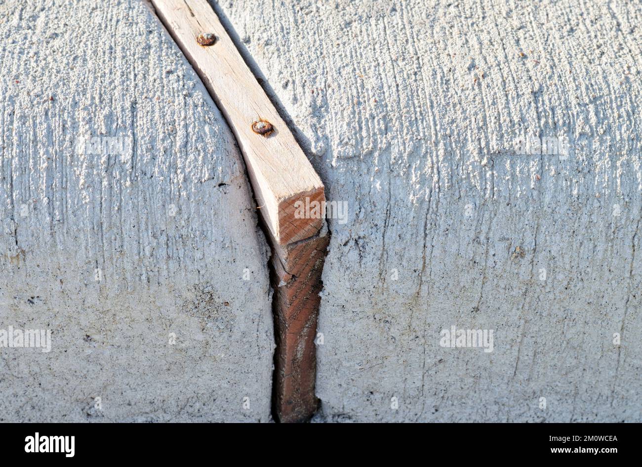Spreizfugen aus Holz trennen Betonabschnitte einer Bordsteinkante, um Belastungen durch wärmebedingte Ausdehnung zu absorbieren. Nahaufnahme auf Bodenhöhe. Stockfoto