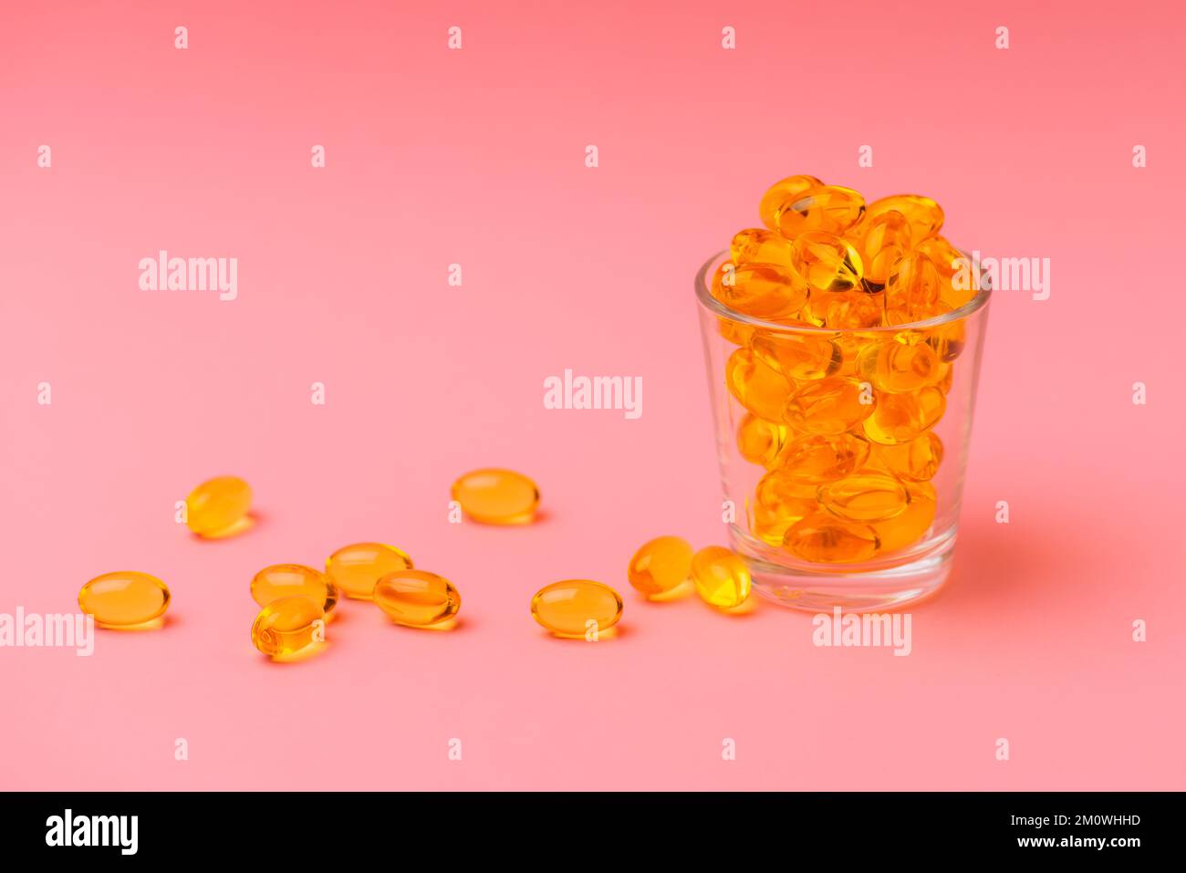 Nahaufnahme von Omega 3 oder Fischölkapseln in einem Glasbecher auf rosa Hintergrund, das Konzept der gesunden Ernährung, Krankheitsprävention und Behandlung Stockfoto